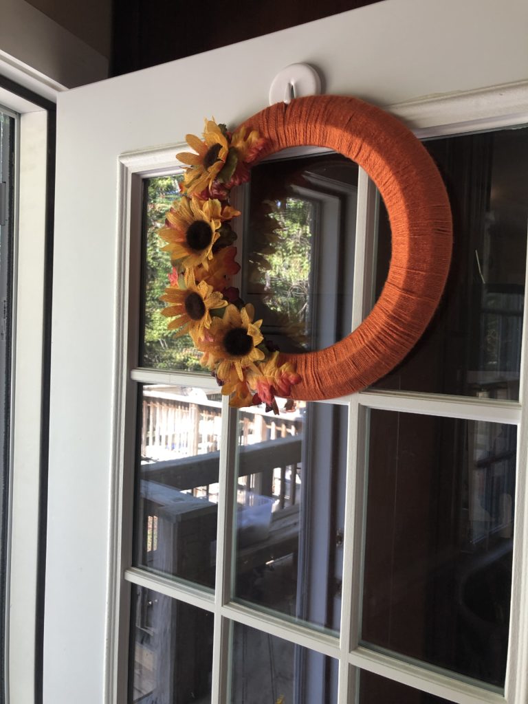 a fall wreath with sunflowers and leaves hanging on a front door