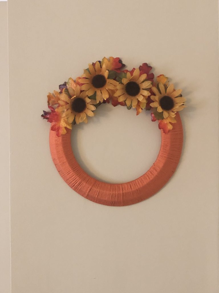 a fall wreath with sunflowers and leaves hanging on a wall