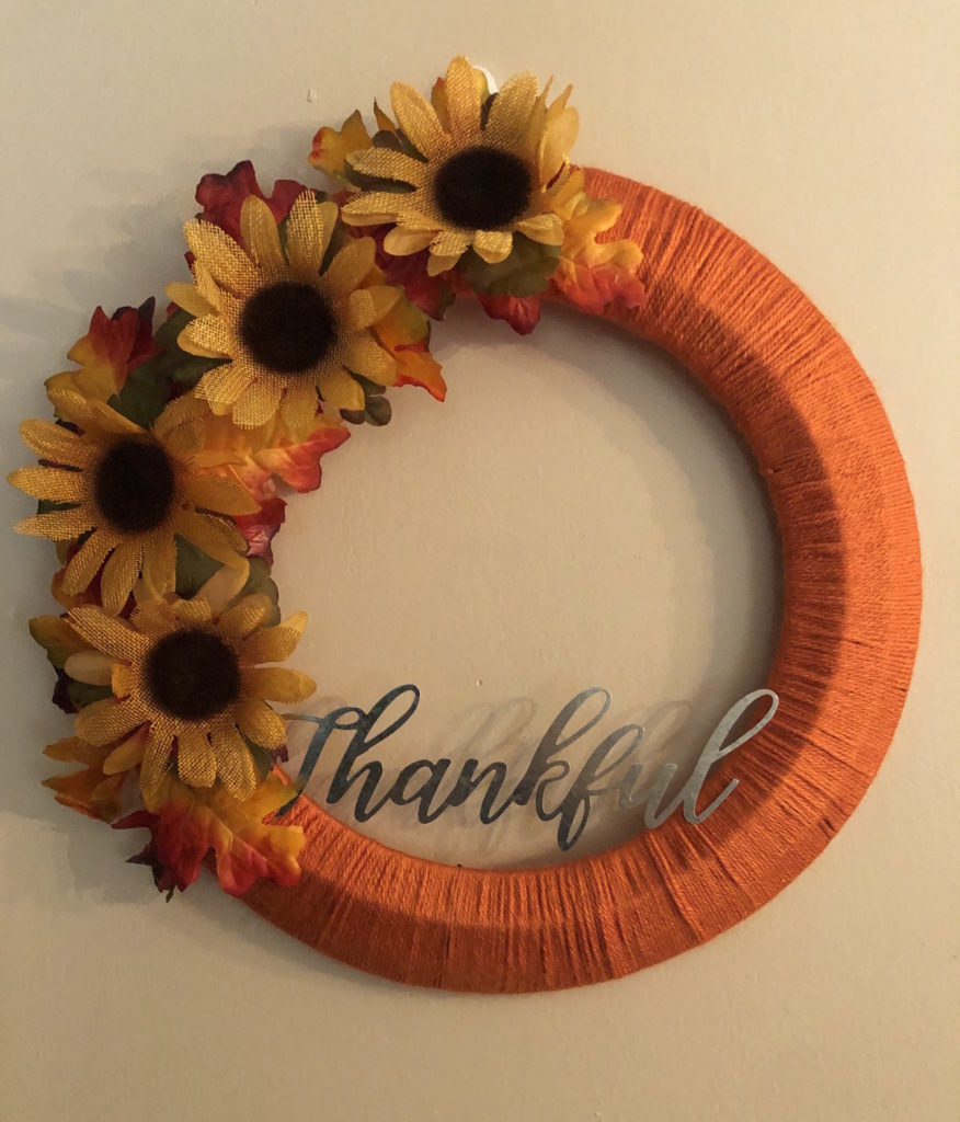 a fall wreath with sunflowers and leaves hanging on a wall with "Thankful" on the bottom