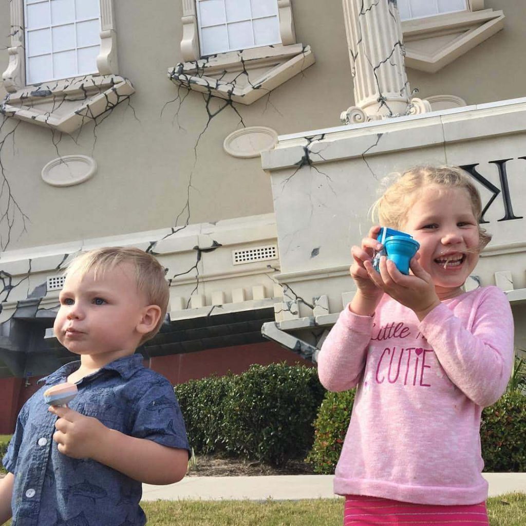 two children eat lollipops outside of an upside down house