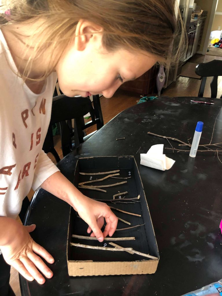 a young girl arranges sticks in a painted black box