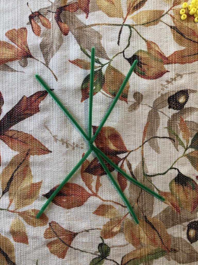 three chenille stems twisted together at the center with pony beads to the side on an autumn tablecloth